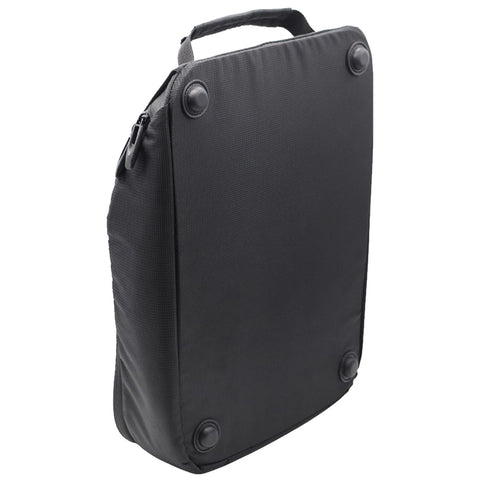 A black rectangular backpack is standing upright on a flat surface with a top handle and four round rubber feet for stability in a minimalistic environment.