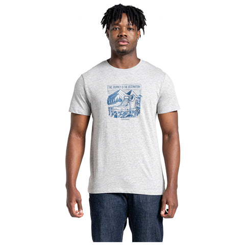 A man stands wearing a gray t-shirt featuring a blue graphic depicting a mountain scene with the text THE JOURNEY IS THE DESTINATION in a casual indoor setting