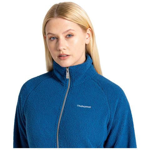 A person with long blonde hair is wearing a blue fleece jacket with a high collar and a front zipper while looking directly at the viewer in a plain white background.