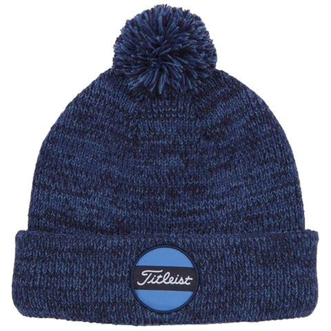 A blue knitted beanie with a pom-pom on top features a logo patch labeled Titleist on the front. The beanie is cozy and suitable for cold weather wear.