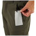 A hand pulls a glasses wipe from a zippered pocket on green pants while the fabric folds around the area, suggesting a casual outdoor environment. The wipe is branded with text.