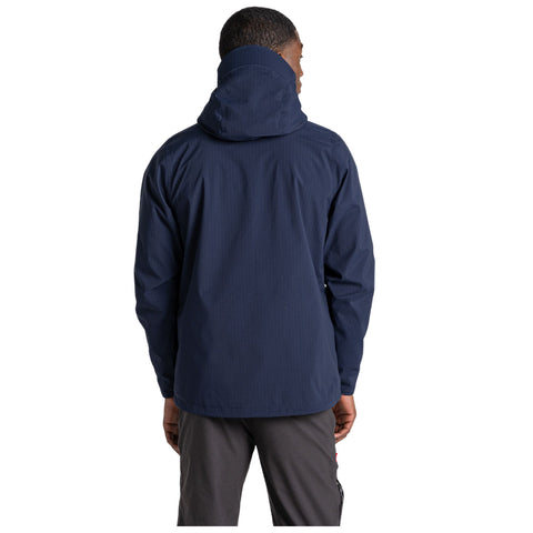 A person stands with their back facing the viewer wearing a dark blue jacket featuring a hood and casual pants in a neutral background. Their hand is slightly visible.