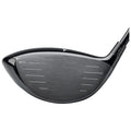 A golf driver is positioned at an angle showing its sleek black clubhead with a metallic face featuring multiple alignment lines for striking the ball effectively. The background is plain and white.