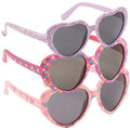 Three pairs of heart-shaped sunglasses are stacked, showcasing playful designs with colorful patterns. The sunglasses have dark lenses and are reflected against a smooth surface below.