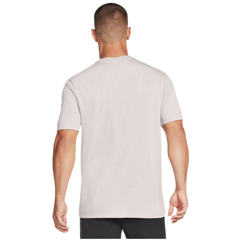 A light-colored t-shirt is worn by a man standing with his back to the viewer in a neutral setting that emphasizes the simple design and fit of the garment.