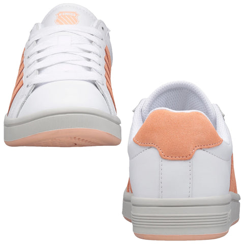 White athletic shoes with peach accents are positioned, featuring laces, a textured sole, and a padded collar, presented against a plain background, emphasizing their design and color.