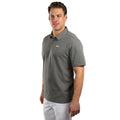 A man stands confidently in a gray polo shirt and white pants showing a relaxed posture and neutral expression against a plain white background