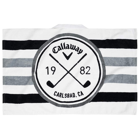 A golf towel features a circular logo with crossed golf clubs at its center displaying the text Callaway 1982 Carlsbad CA surrounded by horizontal black and gray stripes.