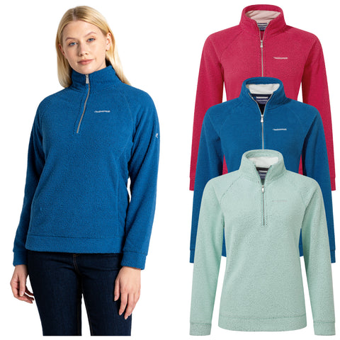 A woman is wearing a blue fleece pullover featuring a half-zip design while three additional pullovers in pink and mint are displayed behind her against a plain background.