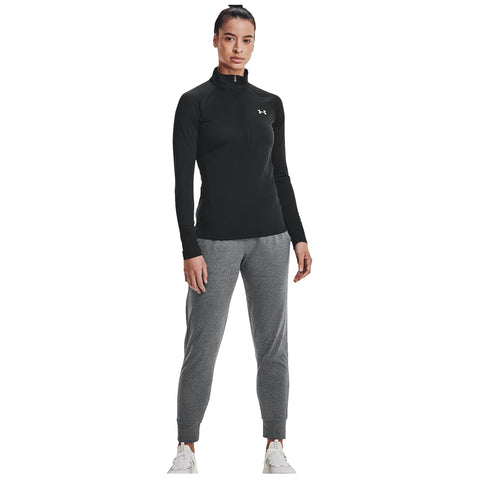 A person stands confidently wearing a black long-sleeve athletic top and gray sweatpants in a minimalistic space with a white background creating a focus on their activewear attire.