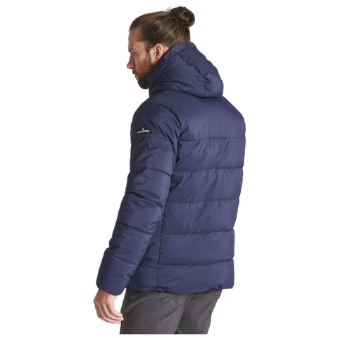 A man stands with his back turned, wearing a navy blue puffy jacket with a hood. He has long hair tied in a bun and is in a neutral setting.