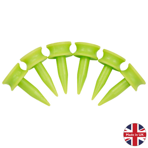 Six bright green golf tees are arranged in a row with pointed tips facing downward suggesting their use for securing golf balls in place on a grassy surface.