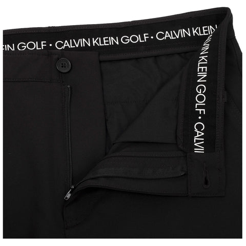 Black golf pants are displayed with an unzipped fly showcasing the interior fabric the waistband features a logo band that reads CALVIN KLEIN GOLF in white lettering.