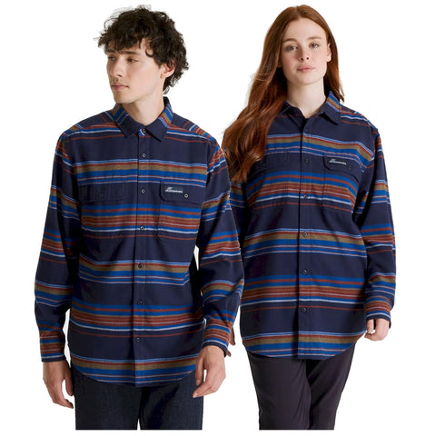 Two individuals stand side by side wearing matching long-sleeve shirts with blue and striped patterns featuring red orange and brown colors in a neutral background.