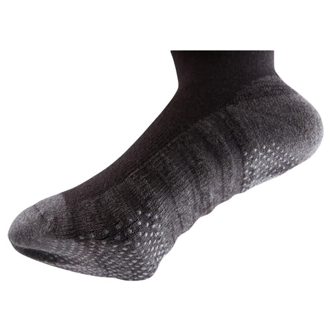 A black sock is positioned with the heel facing upward showcasing a textured design and dotted grip on the sole indicating it's intended for active use or sports settings.