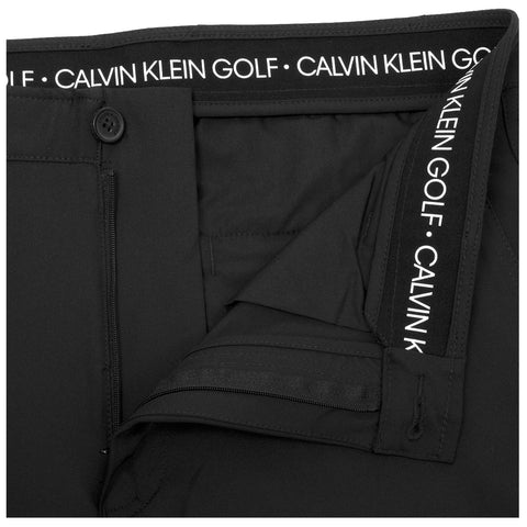 A pair of black golf pants is displayed with an unzipped fly and waistband showing white printed logo. The fabric appears smooth and tailored, emphasizing a sporty design.