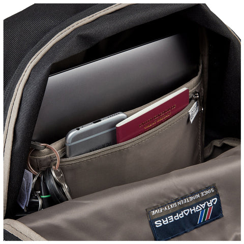 A backpack contains a laptop sitting in its main compartment with a smartphone and a passport visible in an inner pocket while keys hang from a small loop.