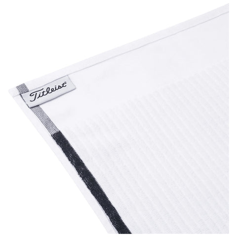 A white golf towel with a textured surface rests at an angle displaying a Titleist logo tag in the corner the background is plain and unobtrusive.