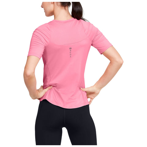 A person stands with their back facing the viewer wearing a pink athletic shirt and black leggings while placing their hands on their hips in a neutral setting.