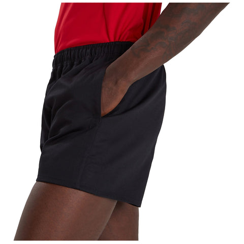 A person wearing black athletic shorts has their hand in the pocket while standing. The upper body is partially obscured, and a red shirt is visible above the shorts.