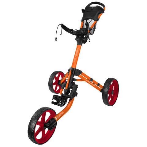 A three-wheeled golf cart in vibrant orange and red is positioned upright with distinct tires and a handle for steering, designed for transporting golf clubs across a course.