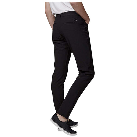 Black trousers are worn by a person standing with a slight turn showcasing the back view while wearing black shoes in a neutral background.