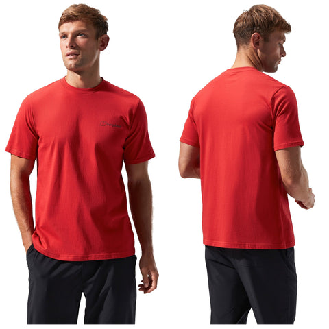 A man stands wearing a bright red t-shirt with short sleeves featuring a logo on the front his expression is neutral as he gazes slightly upward against a plain background.