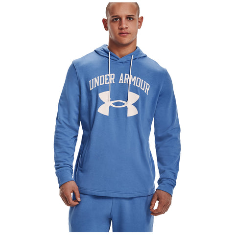 A young man stands confidently wearing a blue hooded sweatshirt with the logo Under Armour prominently displayed on the front against a plain white background. His expression is serious.