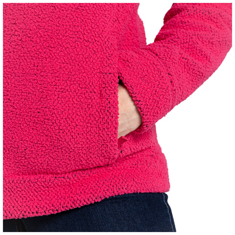 A bright pink fleece top is seen with a hand partially placed in its side pocket while standing against a neutral background, emphasizing the garment’s texture and color.