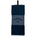 A golf towel hangs vertically featuring a textured hexagonal pattern at the top a plain middle section with the text "Callaway" and a solid plush bottom in dark blue surrounded by a light background.