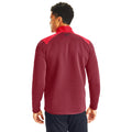 A man is standing with his back turned wearing a maroon long-sleeve shirt with red accents in a well-lit area likely for athletic wear.