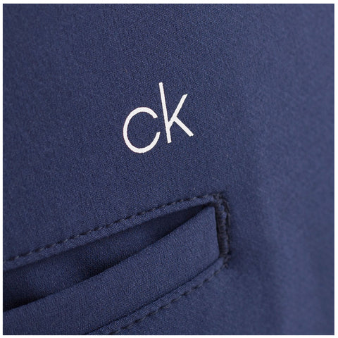 A dark blue fabric features a white logo reading "ck" stitched onto it next to a small pocket showcasing the clothing's design detail in a textile context.